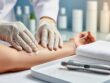 Therapist’s gloved hands applying serum to a client’s arm in a clean spa treatment room next to an RF microneedling device.