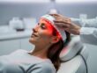 An adult receiving low-level laser therapy in a clinic while a red light applicator targets the scalp.