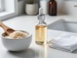 Close-up of a white vanity countertop with a bowl of sugar exfoliating scrub and a glass dropper bottle with cotton pads for chemical exfoliation.