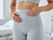 A person’s hands adjusting a FibroGuard post-liposuction compression garment on their torso in a bright clinical recovery room, emphasizing proper fit and comfort.